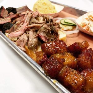 A diverse barbecue platter from Central City BBQ featuring a variety of smoked meats, creamy mashed potatoes, and vegetables, capturing the essence of New Orleans BBQ cuisine.